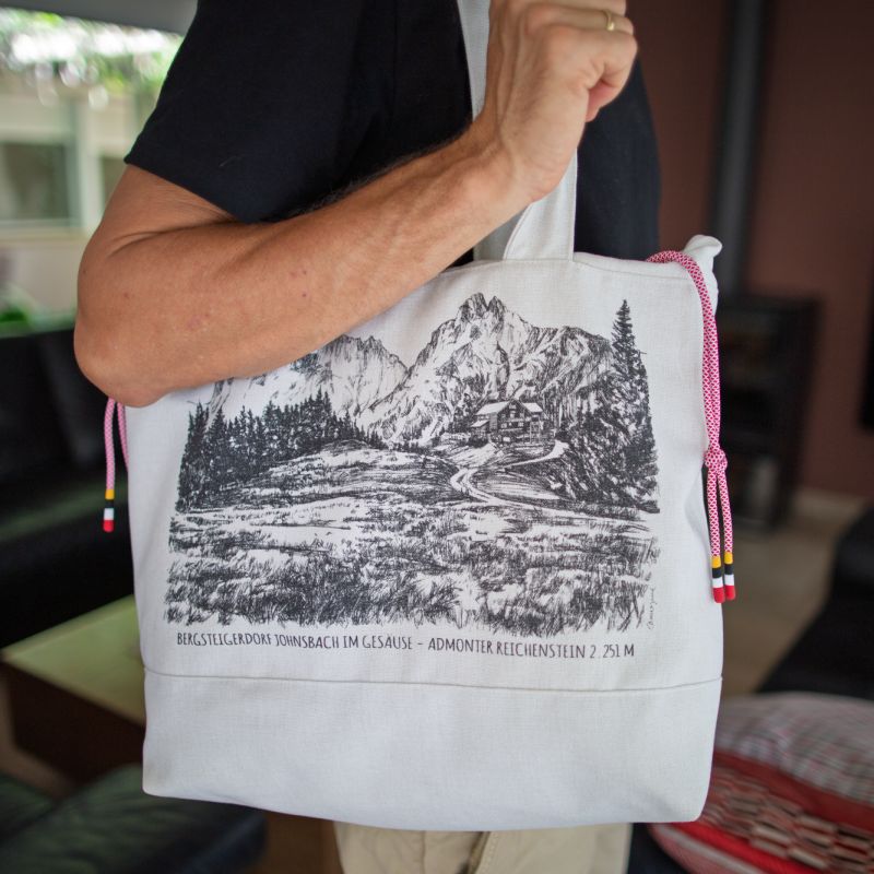 Person carrying a white shoulder bag with an Alpine landscape print