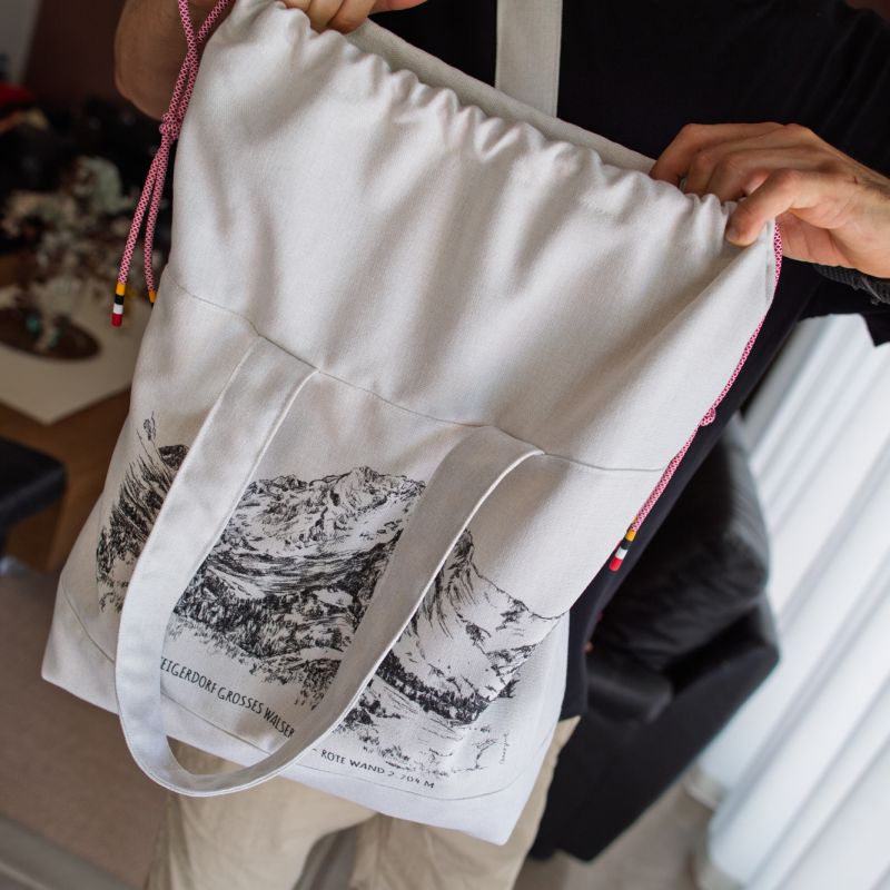 Person holding a large white fabric bag with a printed mountain scene