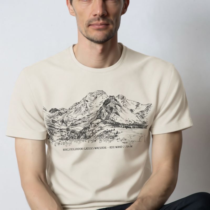 Seated male model wearing a white T-shirt with original mountain artwork