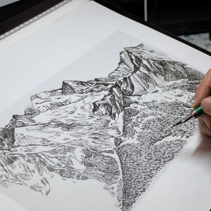 Artist adding fine details to an original mountain landscape drawing on a digital drawing surface