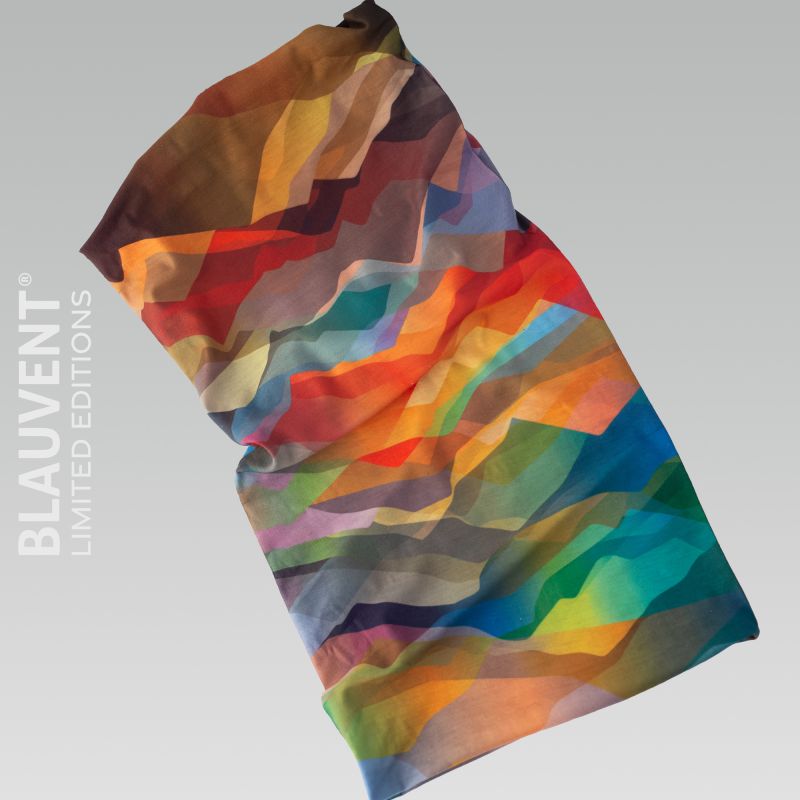 Flat tubular neckwarmer with layered abstract shapes in orange, teal, blue and yellow.