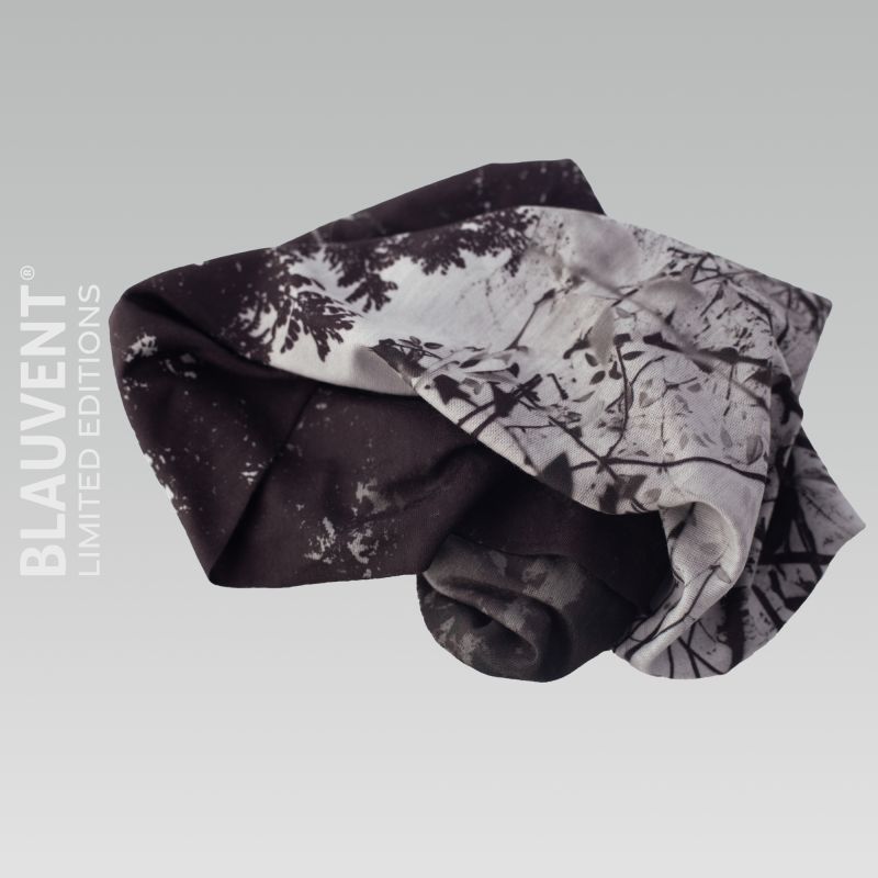 Folded black-and-white forest-print multifunctional neckwarmer showing layered branches.